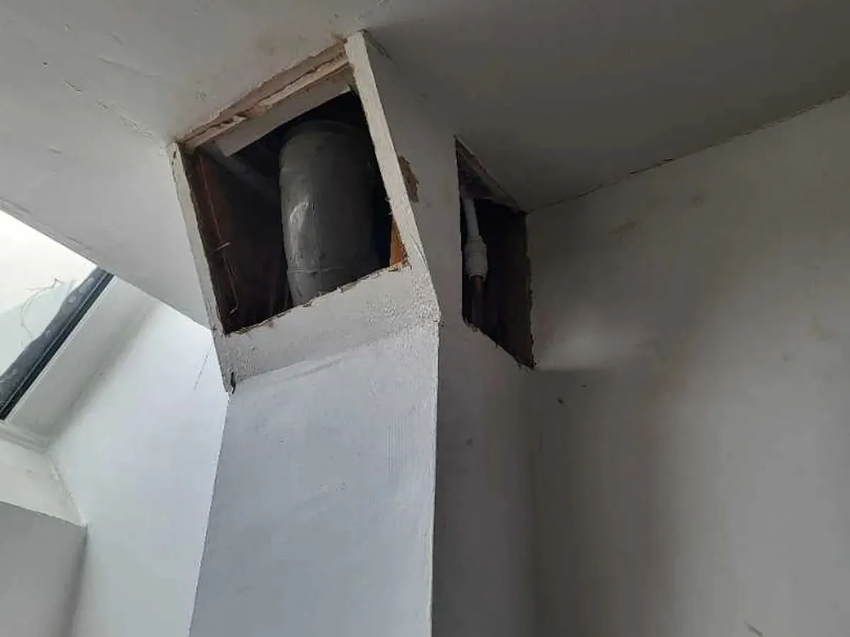 Two rectangular access openings high in white kitchen boxing expose the pipe route inside