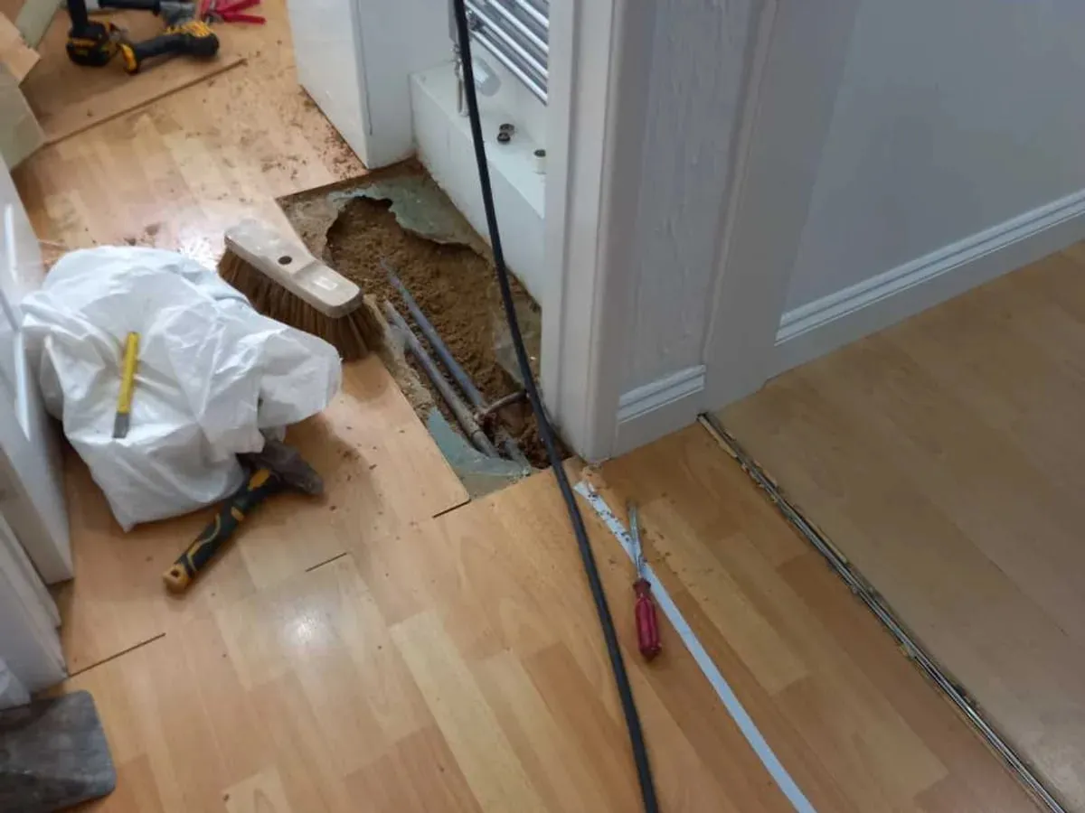 Flooring opened along a hallway and WC doorway exposes the pipe route beneath the screed