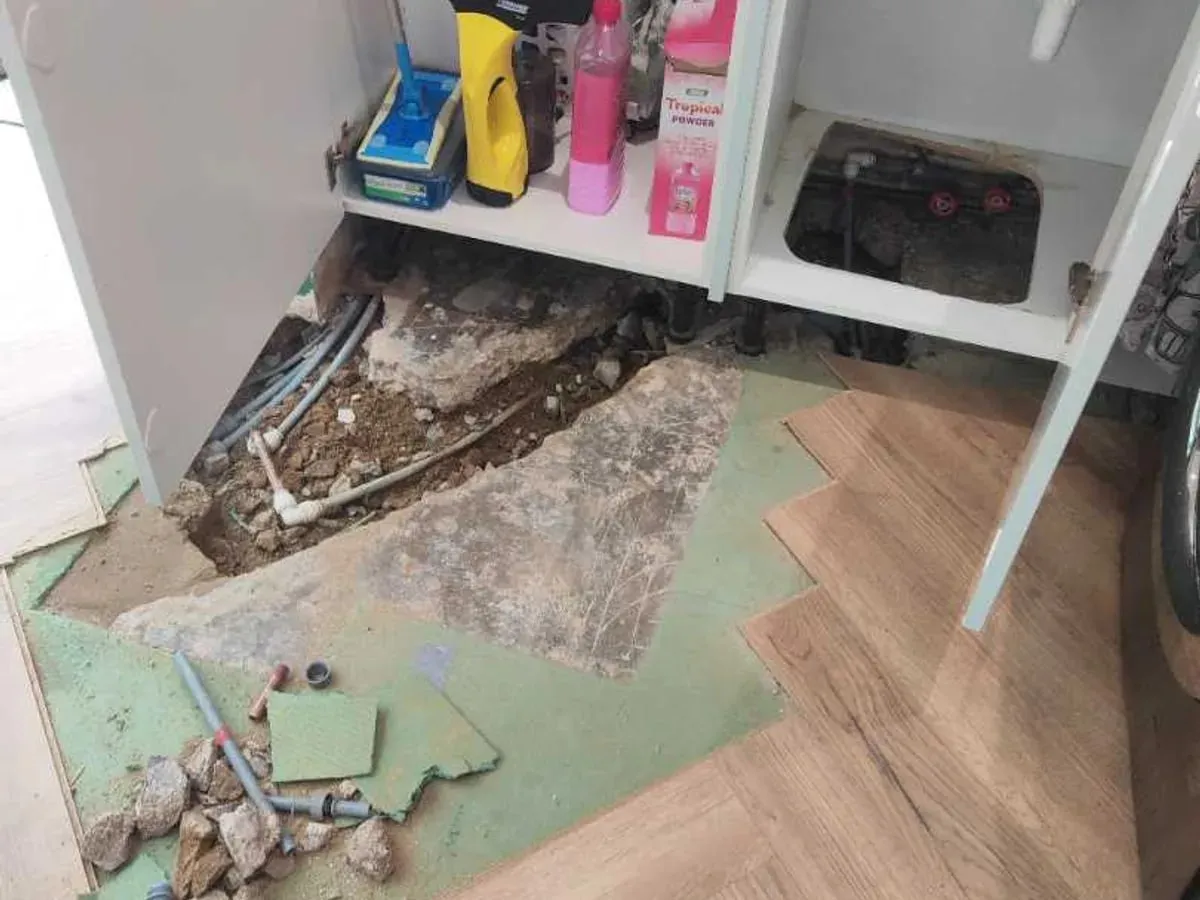 Opened flooring and screed beneath a kitchen sink unit reveal the concealed pipe route