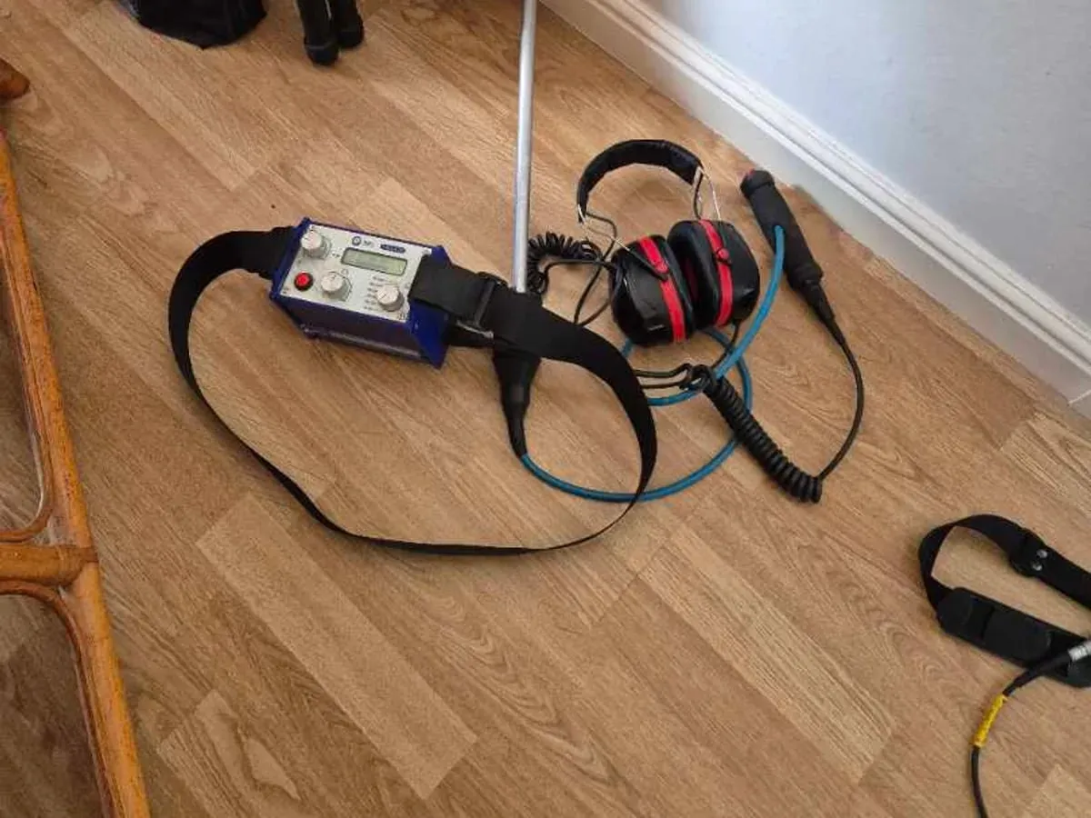 A listening stick, blue amplifier and red headphones laid out on a wood-effect floor