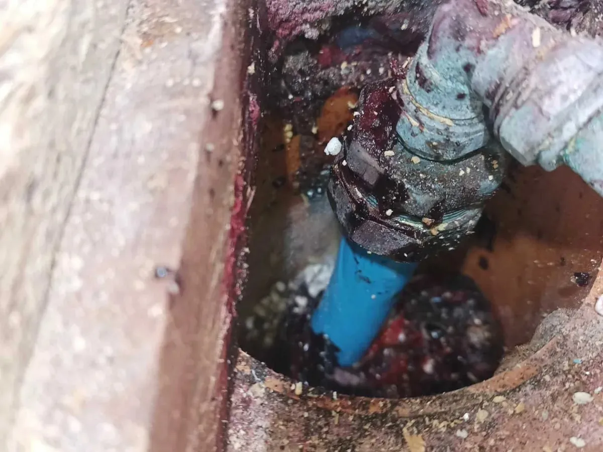 Close-up of a blue supply pipe and corroded connection inside the floor opening